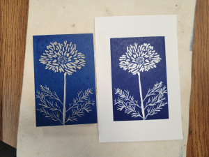photo showing a dandelion carved into a linoleum block and a piece of paper with the image printed in blue